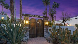 Una verja de madera con un letrero que dice "End of the Trail" que da a un edificio con un muro de piedra y cactus.