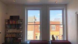 A room with a large window, a bookshelf, and a cat sitting on a bench. - The Bakery Loft in Blairsville (Blairsville)