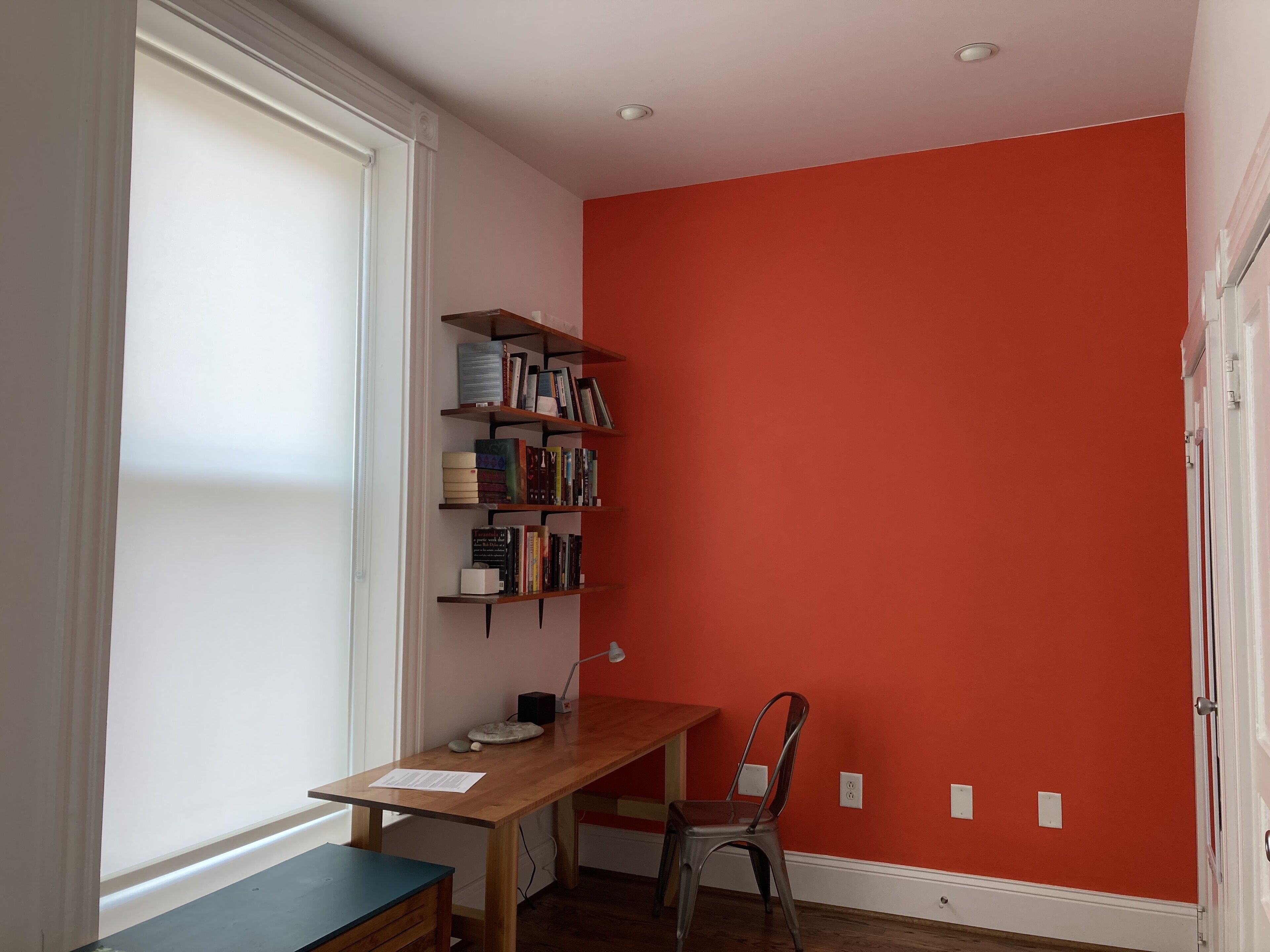A room with a wooden desk, a chair, and a bookshelf against a red wall.