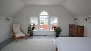A bedroom with a large arched window, a wooden chair, a dresser, and two potted plants. - The Bakery Loft in Blairsville (Blairsville)