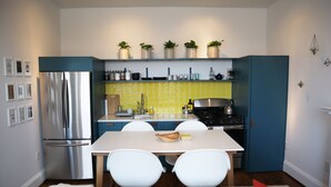 A compact kitchen with a stainless steel refrigerator, a dining table with two chairs, and a blue cabinet. - The Bakery Loft in Blairsville (Blairsville)