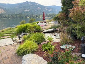 A patio with outdoor furniture, a red umbrella, and a view of a lake and mountains.