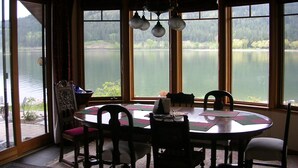 A dining area with a round table, chairs, and a view of a lake through large windows.