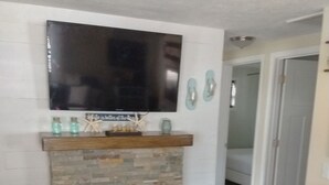 A living room with a stone fireplace, a flat-screen TV mounted above it, and a wooden floor. - Keys cottage -walk to the strip,Private lot, 2bdr 3rd guestroom detached.Spire (Geneva)