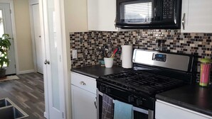 A modern kitchen with white cabinets, a black microwave, a gas stove, and a tiled backsplash. - Keys cottage -walk to the strip,Private lot, 2bdr 3rd guestroom detached.Spire (Geneva)