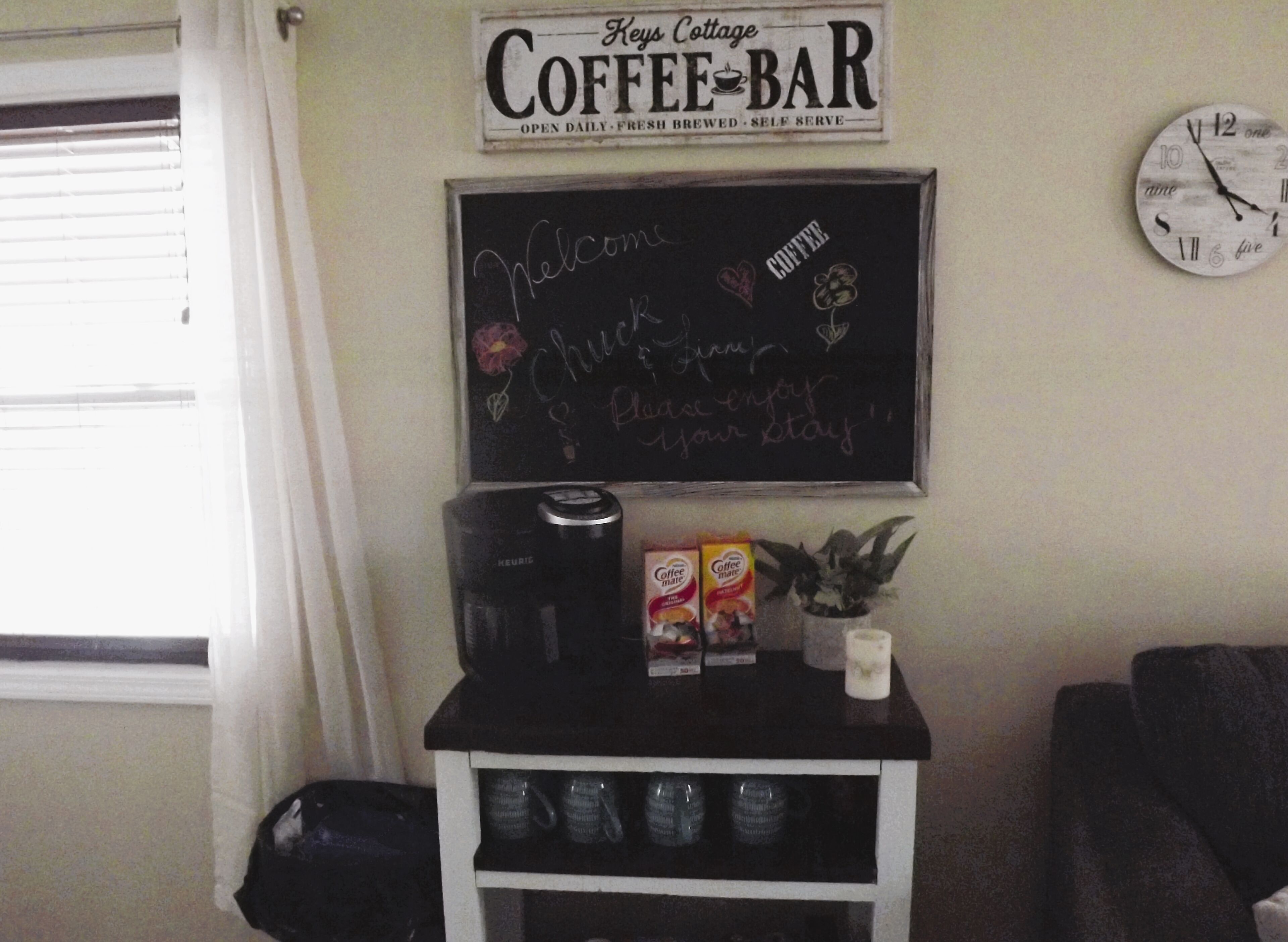 Kahvilanurkkaus, jossa on kyltti, jossa lukee ”Keys Cottage Coffee Bar”, liitutaulu, jossa on tervetuliaisviesti, kahvinkeittimiä ja pakattuja kahvipaketteja.