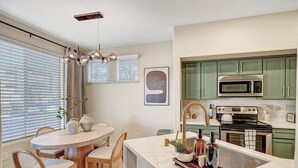 Une cuisine moderne avec des meubles de couleur verte, un four à micro-ondes en acier inoxydable, une cuisinière et un évier.