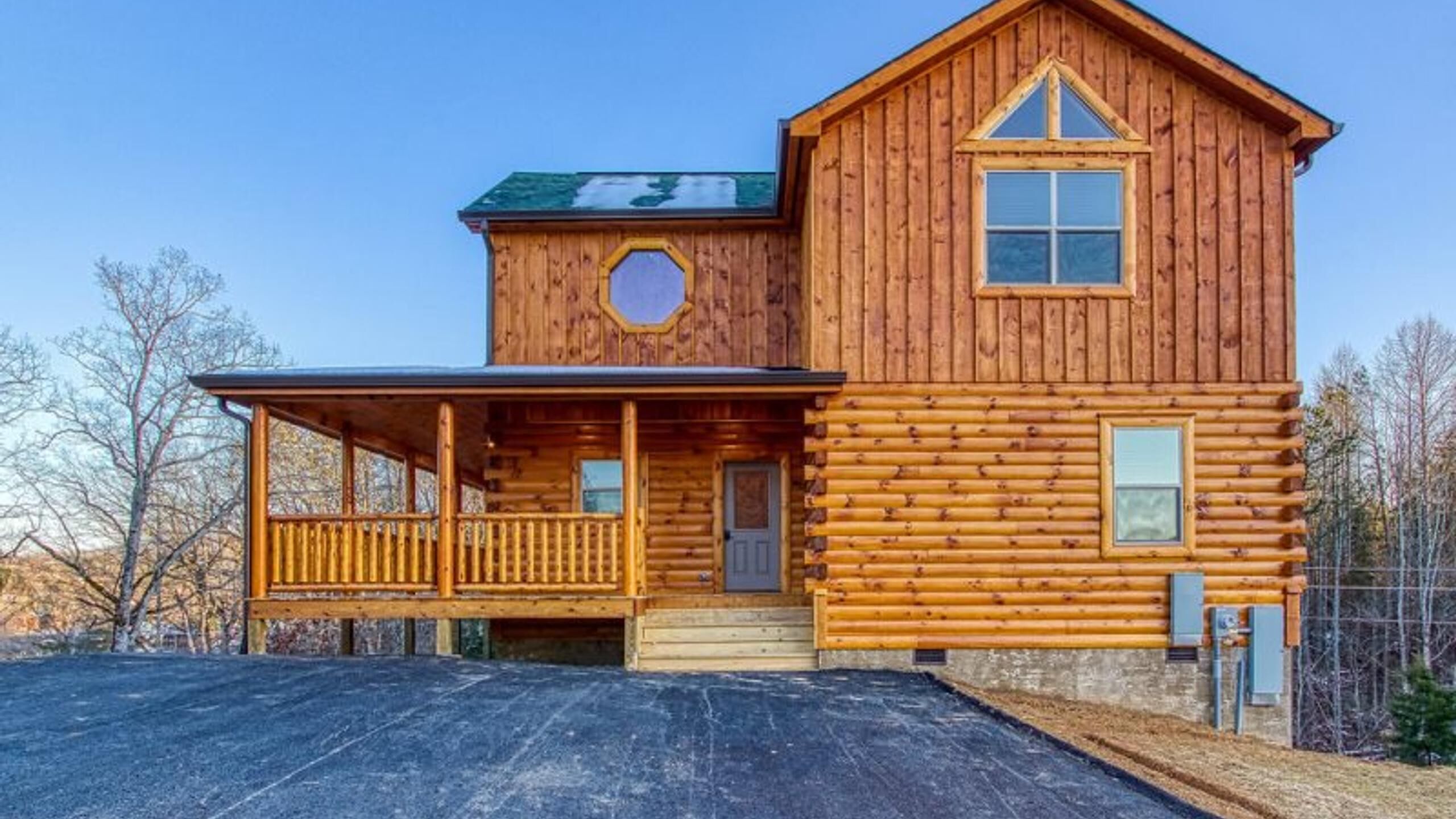 A two-story log cabin with a covered porch and a large window on the upper floor.