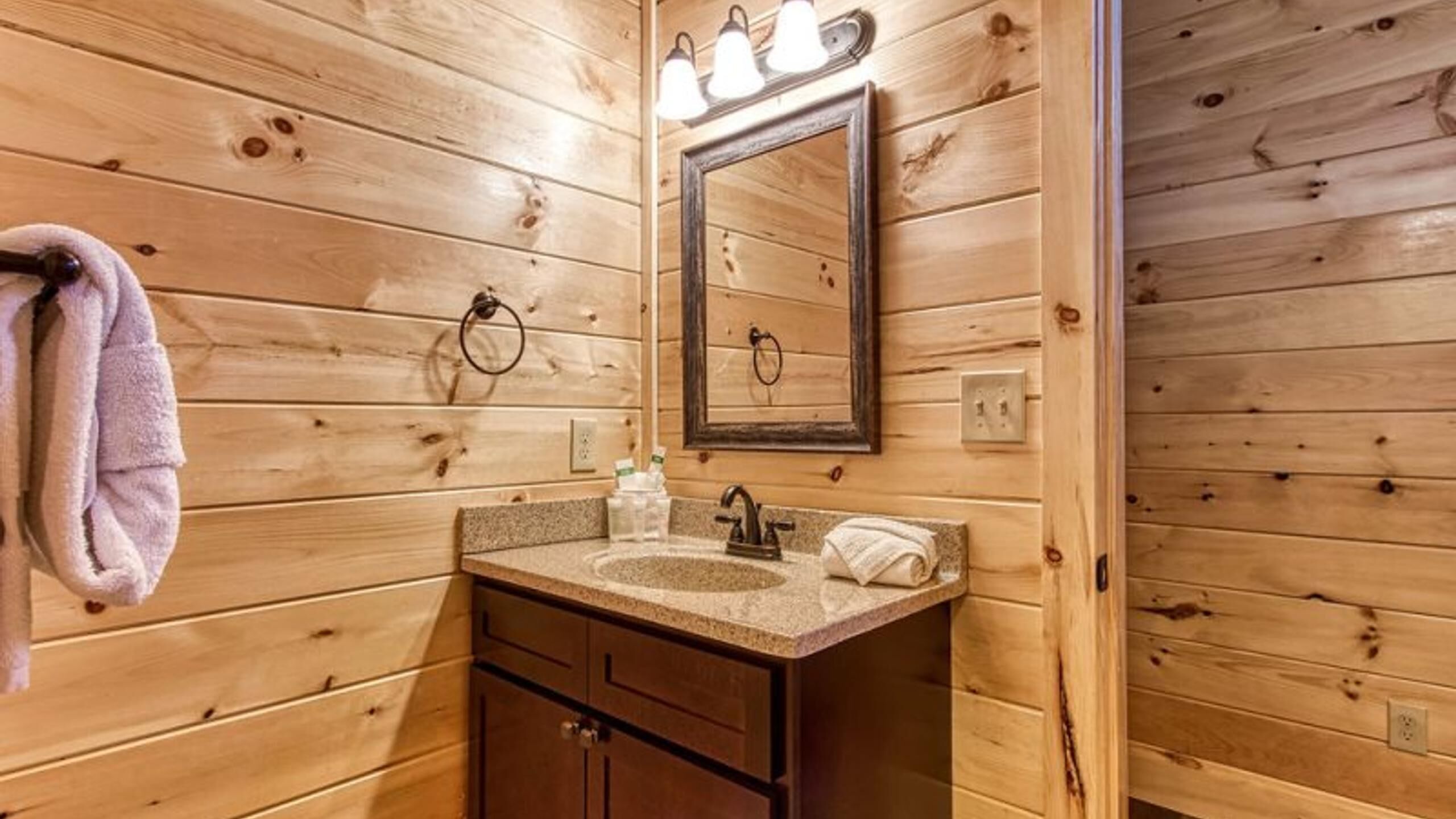 Baño de cabaña de madera con lavabo, espejo y toallero.