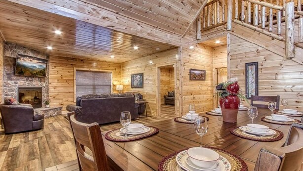 Interior de una cabaña de troncos con comedor, chimenea y escalera.