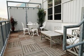 Relax in this outdoor seating area with comfortable chairs and tables, surrounded by lush greenery and a metal railing.