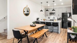 A modern kitchen with white cabinets, a wooden dining table, black chairs, and pendant lights. - Living the Dream #79 by RedAwning (St. George)