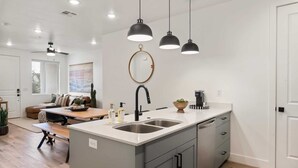 A modern kitchen with a large island, pendant lighting, and a view to the living area. - Living the Dream #79 by RedAwning (St. George)