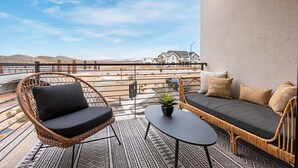 A balcony with wicker furniture, a small table, and a view of a distant building. - Living the Dream #79 by RedAwning (St. George)