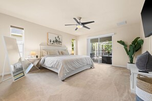 A bedroom with a bed, a ceiling fan, a large window, and a view of the outdoors.