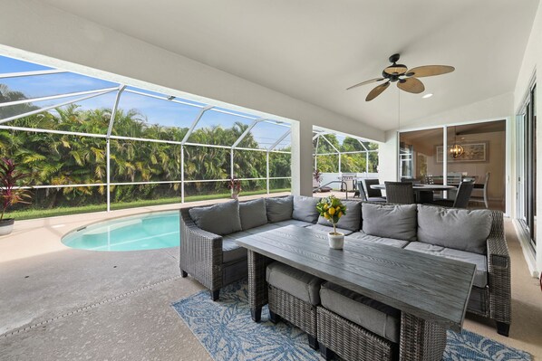 A spacious patio with a pool, outdoor furniture, and a view of lush greenery.