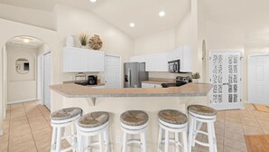 Una cocina moderna con armarios blancos, una isla central con taburetes y una puerta decorativa.