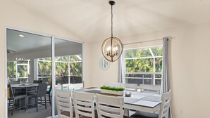Un comedor con una mesa y sillas, un candelabro y ventanas amplias con vistas a la vegetación.