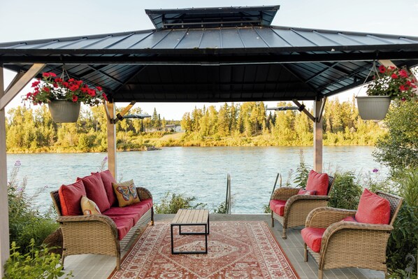 Un espace extérieur abrité, aménagé avec des meubles en osier et offrant une vue sur un lac.