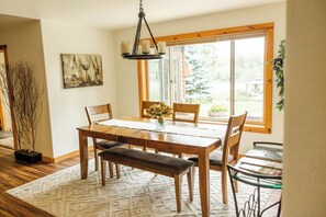 Un coin repas avec une table en bois, des chaises, un banc, un vase de fleurs et un tableau accroché au mur.