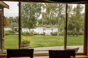 On aperçoit, à travers une porte vitrée, un espace verdoyant avec un kiosque et un petit quai au bord d’un lac.
