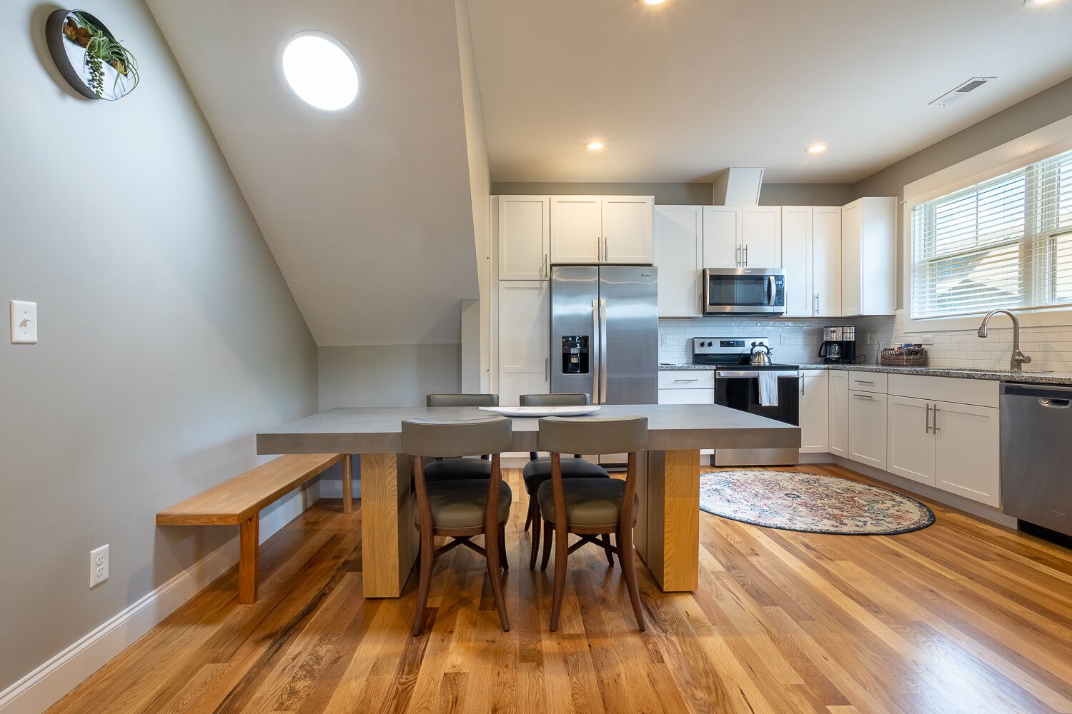 A modern kitchen with a dining area, featuring a large island, built-in appliances, and a view of the outdoors.