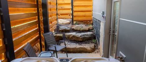 A small outdoor patio area with a wooden fence, a hot tub, and a seating area with chairs and a table.