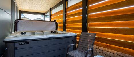 A hot tub with a wooden exterior and a bench, set against a wooden wall with a bench and a small table nearby.