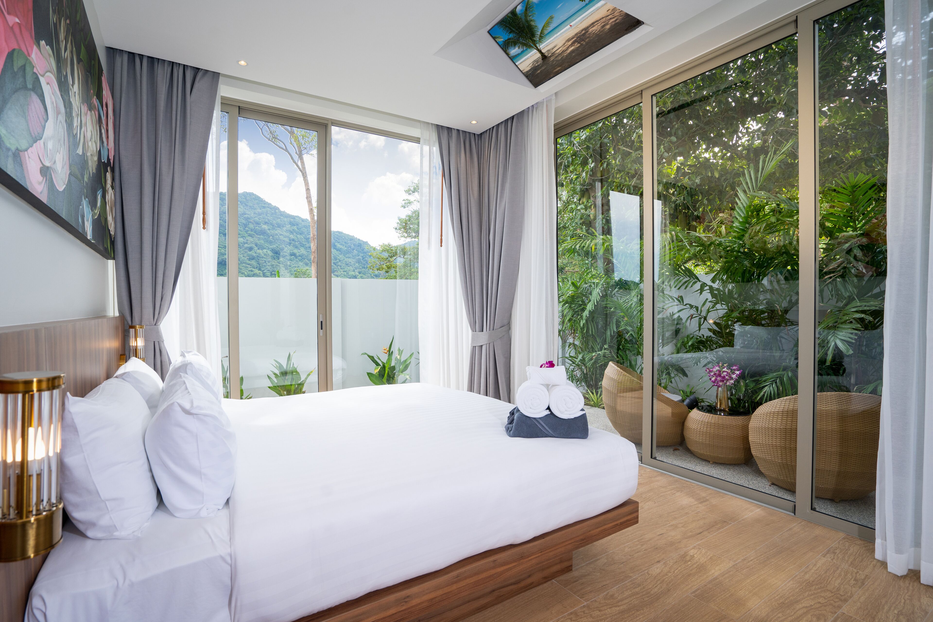 A modern hotel room with a large bed, a view of lush greenery, and a sliding glass door to the outdoors.