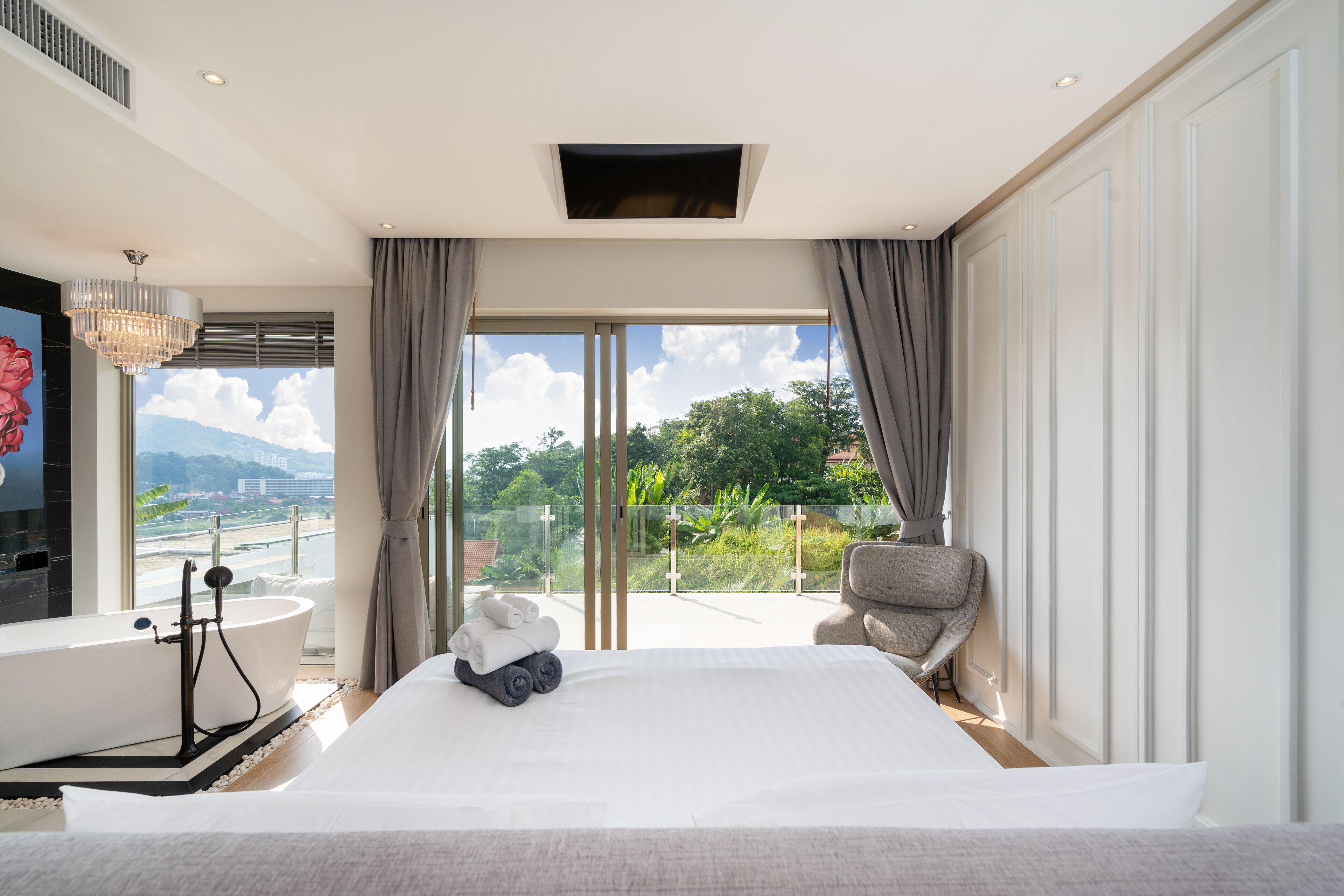 A spacious bedroom with a large bed, a bathtub, and a view of greenery and mountains.
