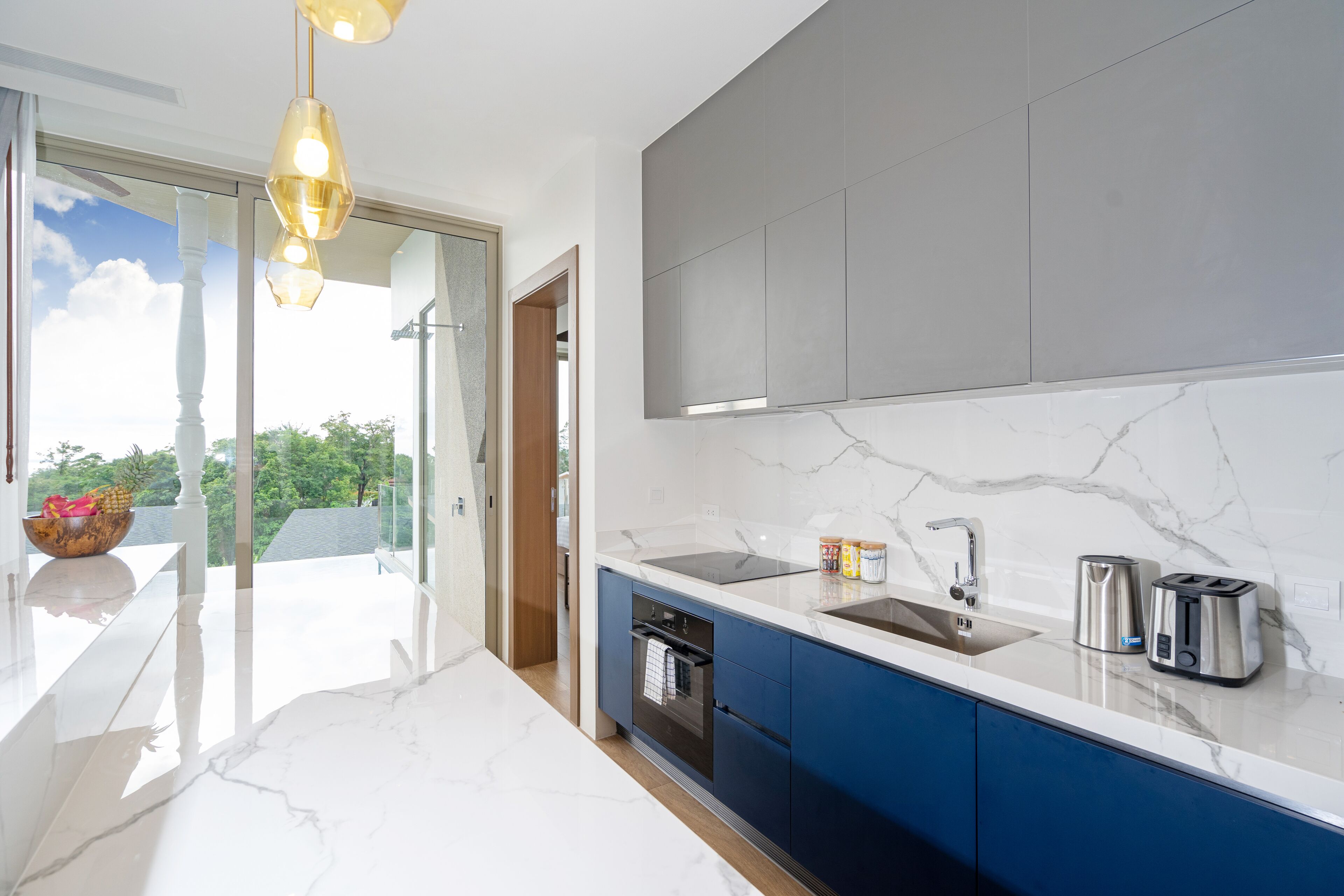 A modern kitchen with a marble countertop, stainless steel appliances, and a view of greenery outside.