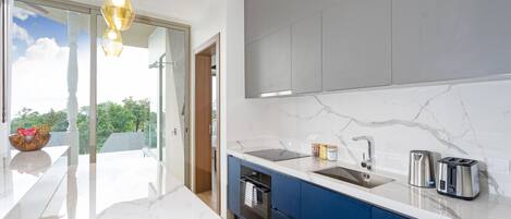 A modern kitchen with a marble countertop, stainless steel appliances, and a view of greenery outside.