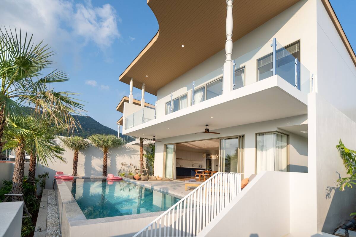 A modern two-story house with a swimming pool, outdoor seating, and a view of the mountains.