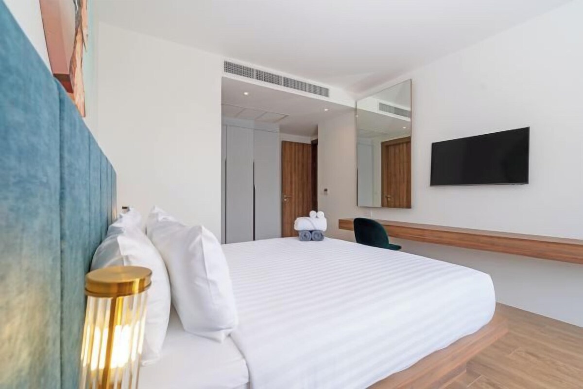 Ein Hotelzimmer mit einem Bett, einem flachbildfernseher an der Wand, einem Spiegel und Holzboden.