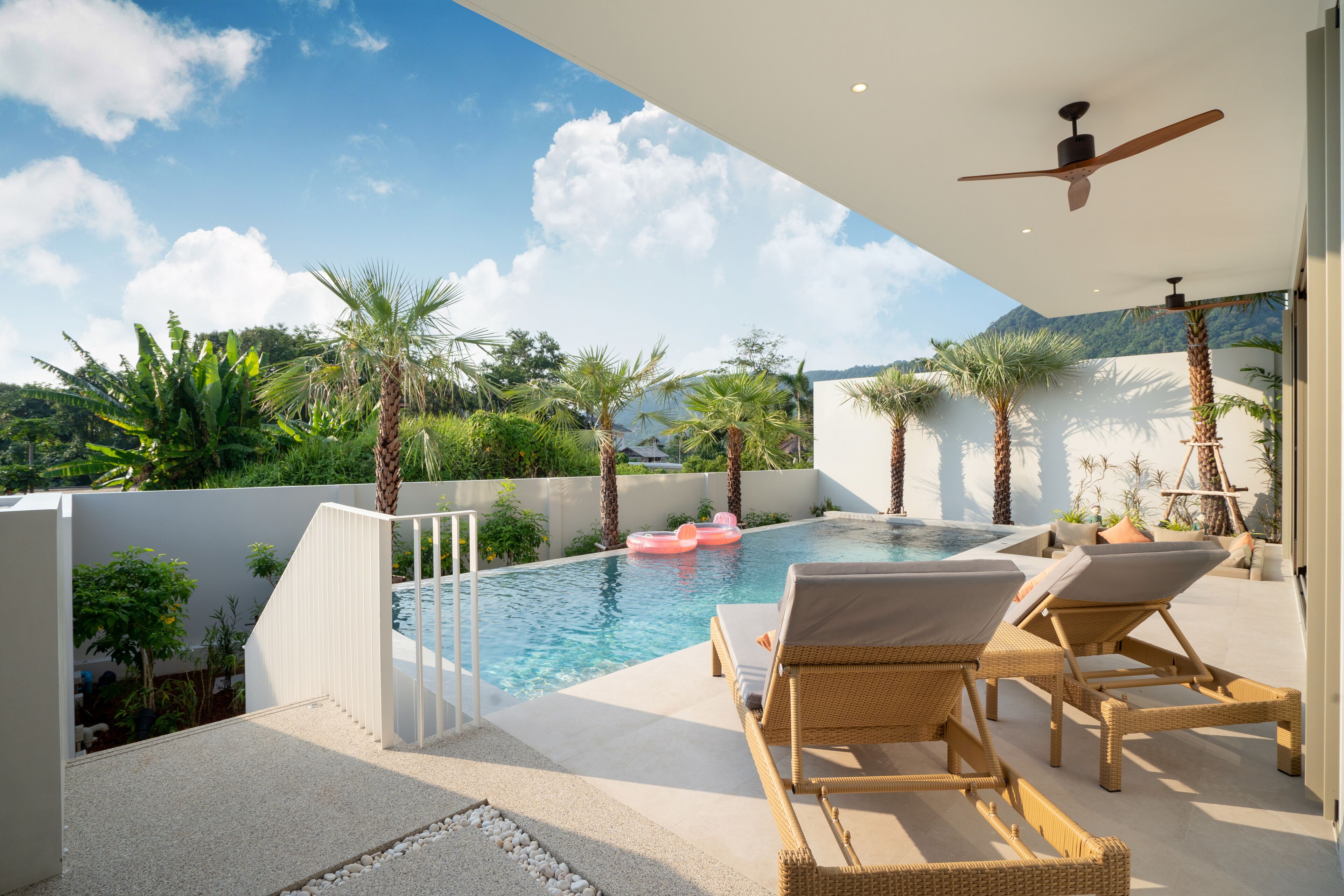 Un espace piscine doté de chaises longues, de palmiers et offrant une vue dégagée sur les montagnes.