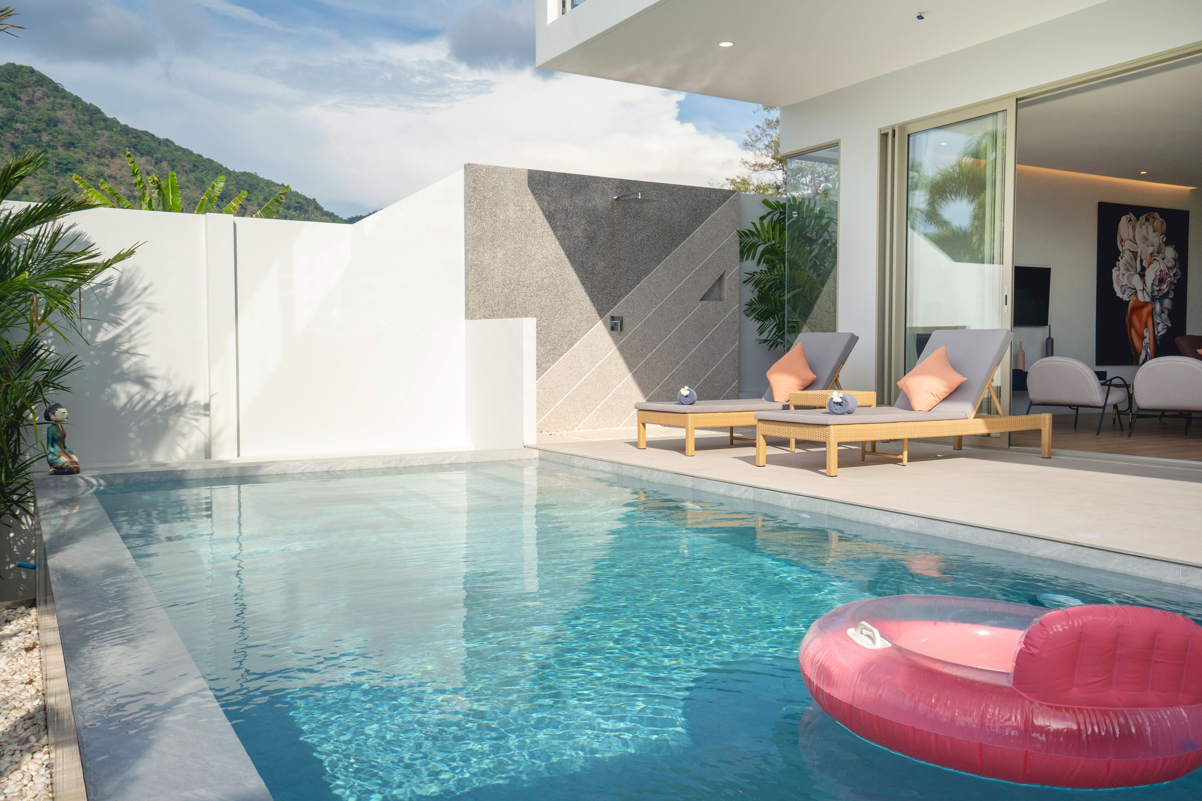 A modern outdoor pool area with clear blue water, lounge chairs, and a view of a mountainous landscape.