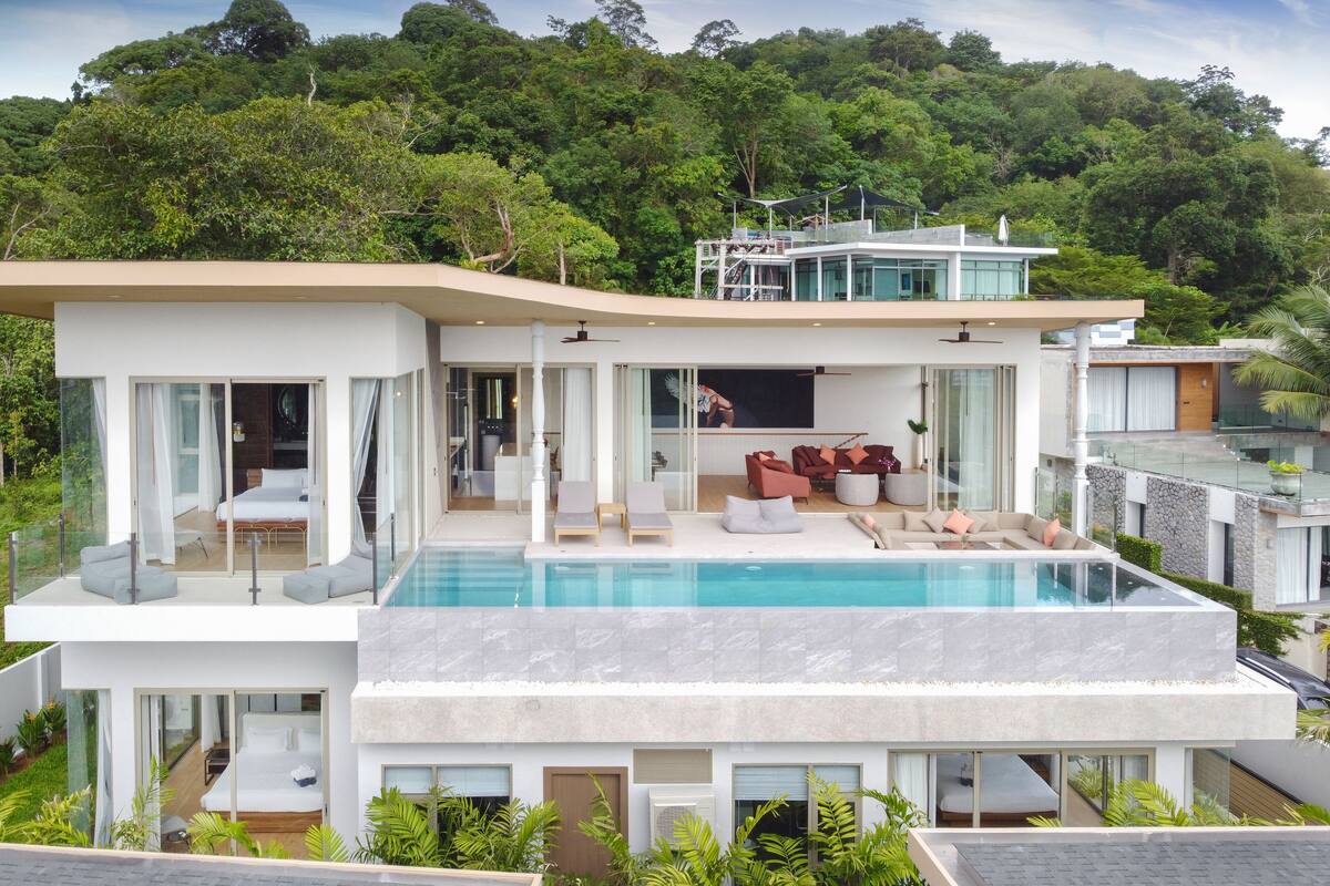 A modern house with a swimming pool, large glass windows, and a balcony overlooking lush greenery.