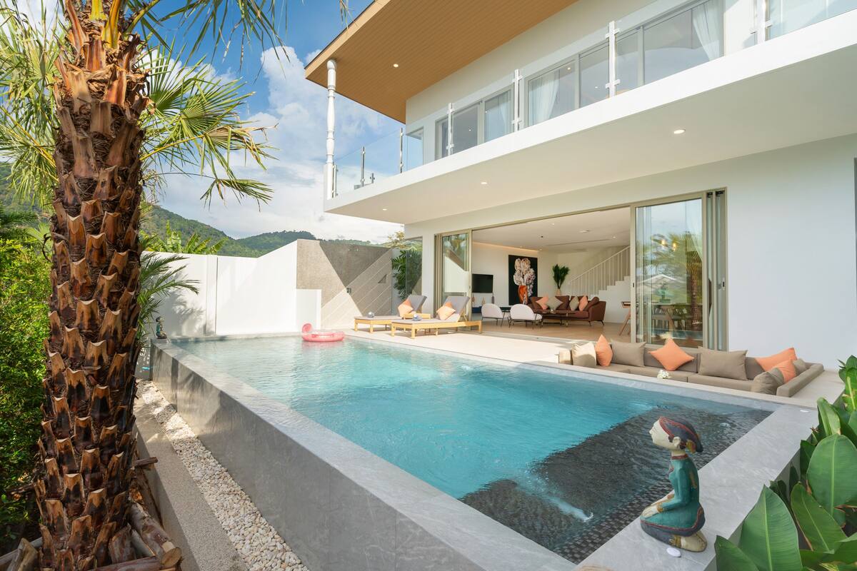 A modern house with a swimming pool, outdoor seating, and a view of the mountains.