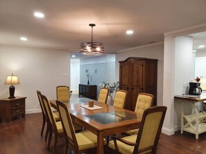 A dining area with a glass-top table, wooden chairs, a chandelier, a cabinet, and a coffee machine.
