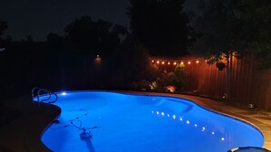 Uma piscina à noite com luzes de Natal e uma cerca de madeira ao fundo.