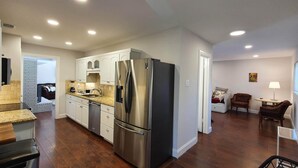 Uma cozinha moderna com eletrodomésticos de aço inoxidável, uma sala de jantar com mesa e cadeiras, e uma sala de estar com sofá e luminária.