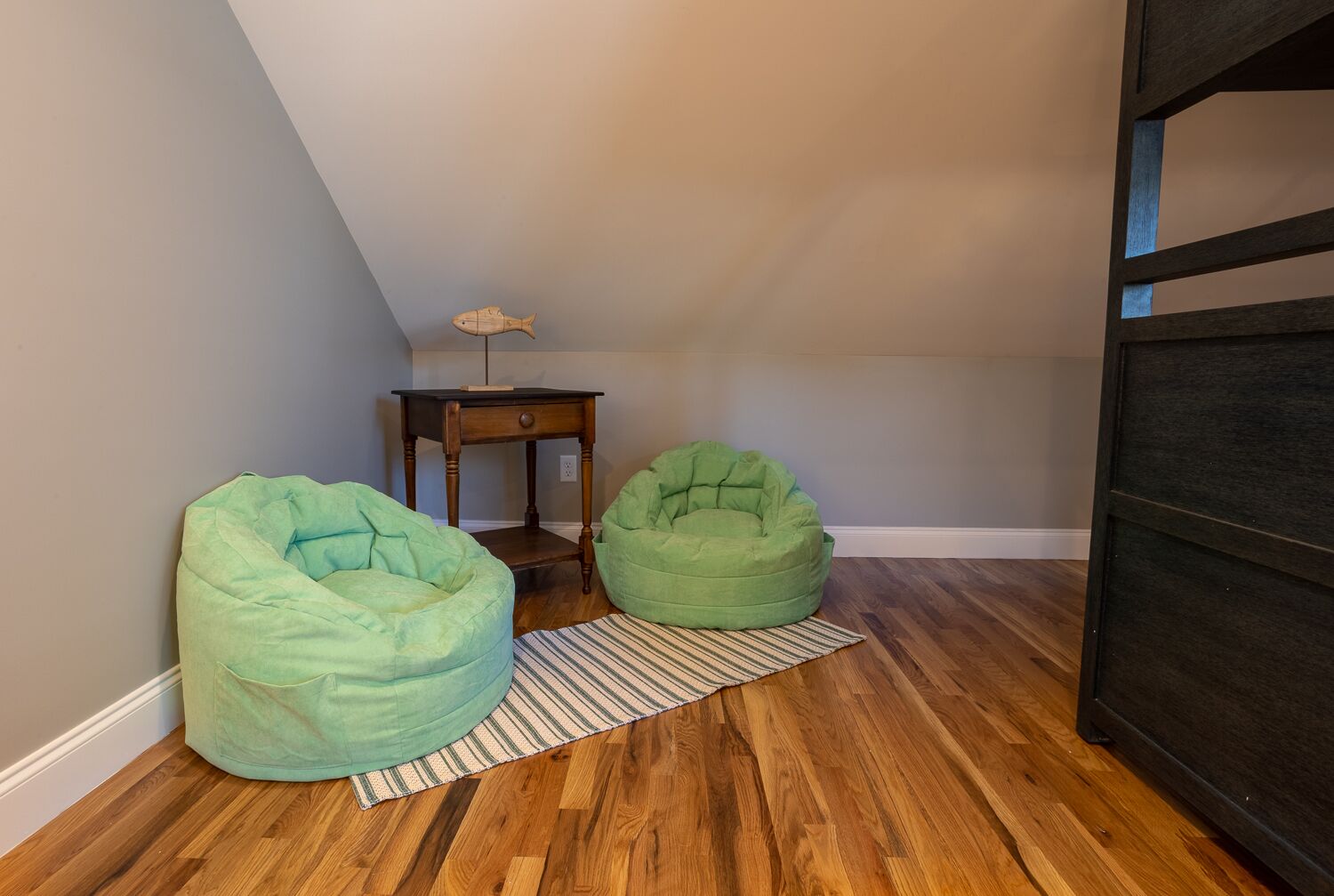 A room with two green bean bags, a small wooden table with a lamp, and a striped rug on a wooden floor.