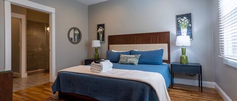 A bedroom with a large bed, two bedside tables, a nightstand, a mirror, and a window with blinds.