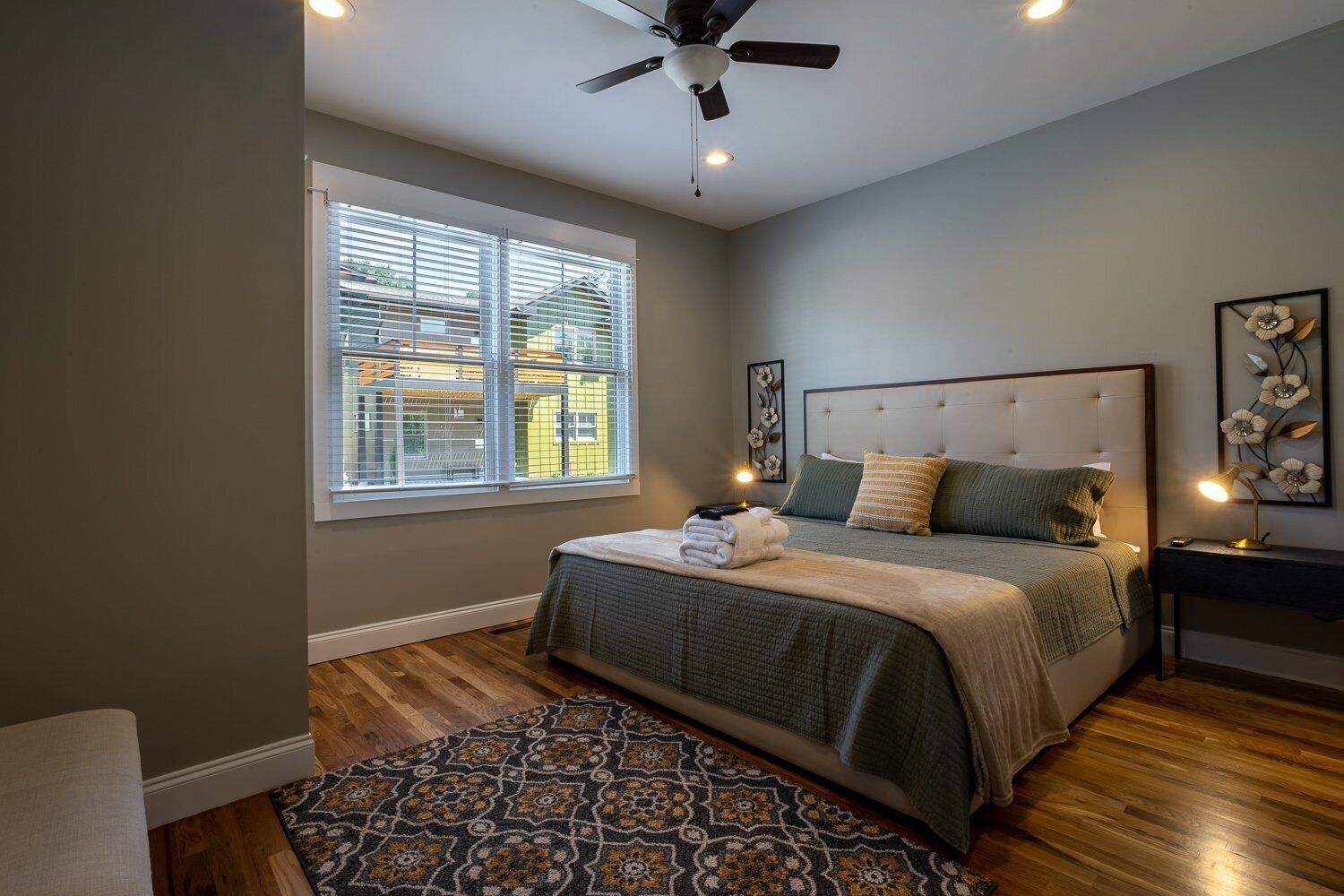 A bedroom with a bed, a nightstand, a ceiling fan, and a window with blinds.