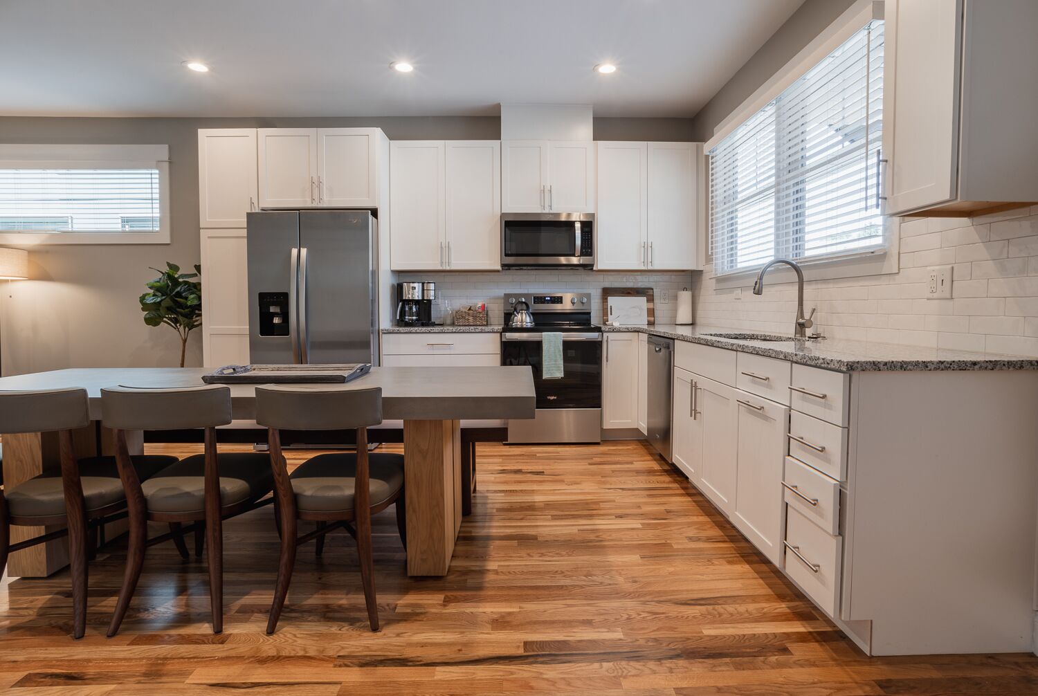 A modern kitchen with white cabinets, stainless steel appliances, and a wooden floor.