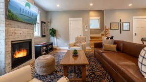 Ein Wohnzimmer mit Kamin, Deckenventilator, Sofa, Couchtisch und einer Treppe.