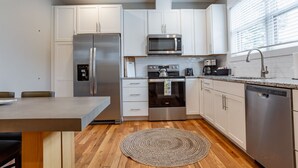 Eine moderne Küche mit weißen Schränken, Edelstahlgeräten, Holzboden und einem Essbereich mit Tisch und Stühlen.