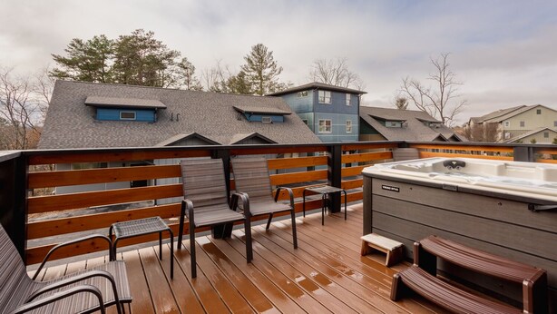Eine Holzterrasse mit Sitzgelegenheit im Freien, einem Whirlpool und Blick auf Wohnhäuser.