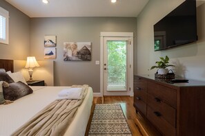 Une chambre à coucher comprenant un lit, une table de chevet avec une lampe, une commode, un téléviseur fixé au mur et une porte avec des stores.