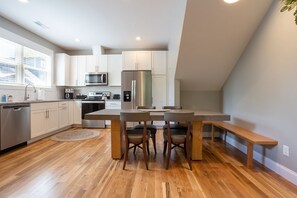 Une cuisine moderne avec des meubles blancs, des appareils en acier inoxydable et une table à manger en bois, accompagnée de quatre chaises.